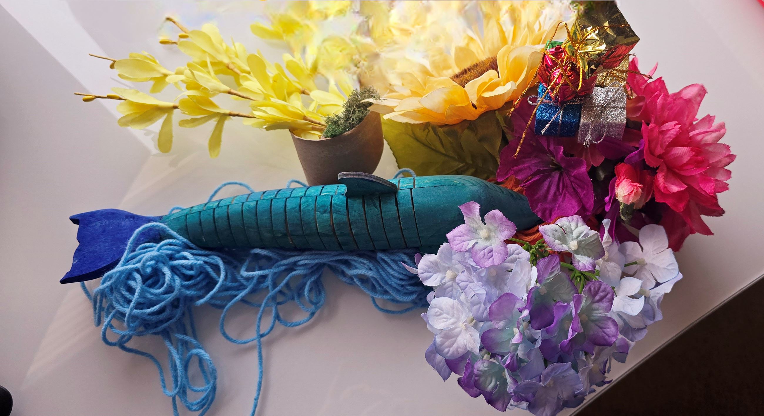 Artificial flowers, blue wooden fish with yarn, and shiny gift boxes